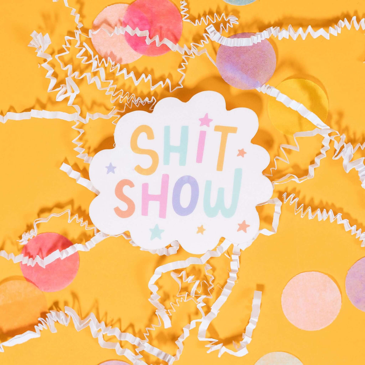 On a sunny mustard background sits a sticker with white crinkle and big, colorful confetti scattered around This white scallop shaped sticker has illustrated stars in pastel colors of purple, pink, orange, mustard yellow, aqua blue, and purple. It says "SHIT SHOW" in handwritten block lettering in pastel colors of purple, pink, orange, mustard yellow, aqua blue, and purple. 2"-3"