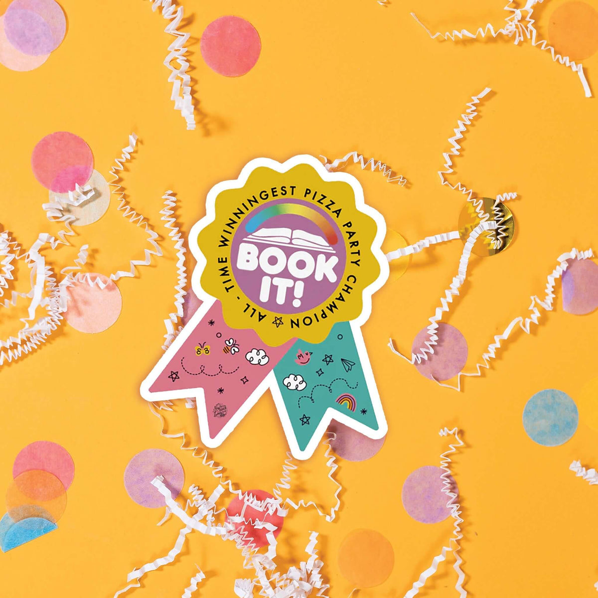On a sunny mustard background sits a sticker with white crinkle and big, colorful confetti scattered around. This colorful ribbon sticker has an illustration of an open book and a rainbow meter above it. It says "BOOK IT!" in a white, bubble text. There are handdrawn doodles on the pink and turquoise ribbons. 'ALL-TIME WINNINGEST PIZZA PARTY CHAMPION'.