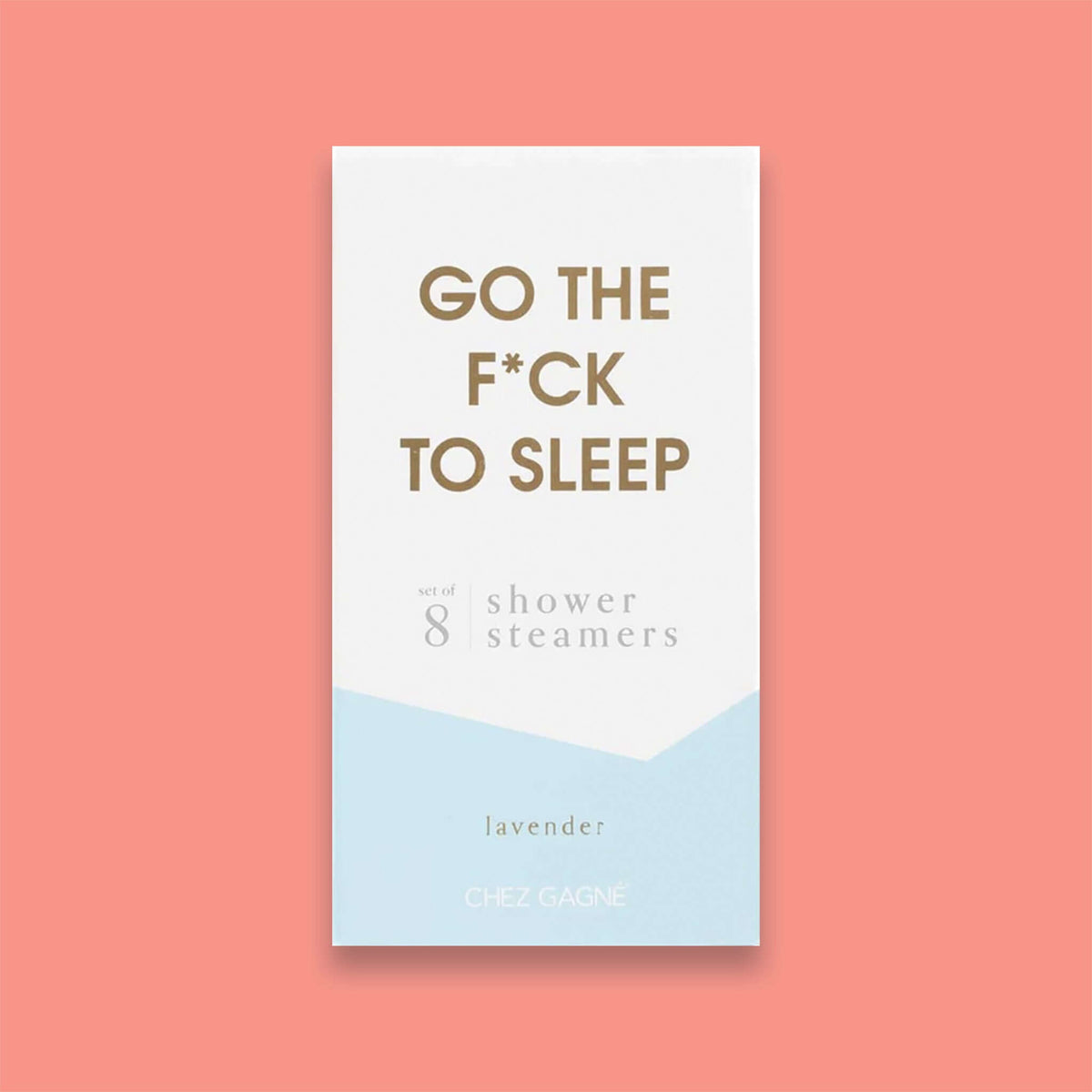 On a light coral background sits a box. This picture is a close-up of a white and light blue package that says "GO THE F*CK TO SLEEP" in gold foil, all caps block lettering. Under it says "set of 8" and " shower steamers" in grey, lowercase serif font. At the bottom it says "lavender" in gold foil, lower case serif font.