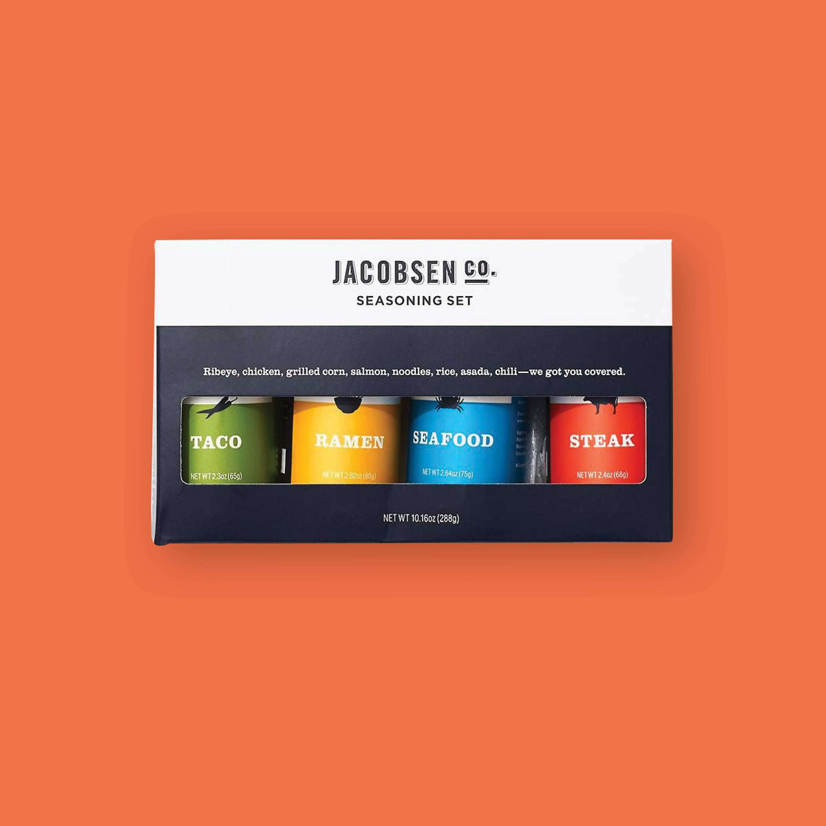 On an orangey-red background sits a box and four jars. The box is black and white with a see-thru window. It says "JACOBSEN CO. SEASON SET" in black, call caps block font. Under it says "Ribeye, chicken, grilled corn, salmon, noodles, rice, asada, chili - we got you covered." in white, sreif font. The bottles are seasons of "Taco" in green label, "Ramen" in yellow label, "Seafood" in blue label, and "Steak" in red label. Each is 2.40z(68g)