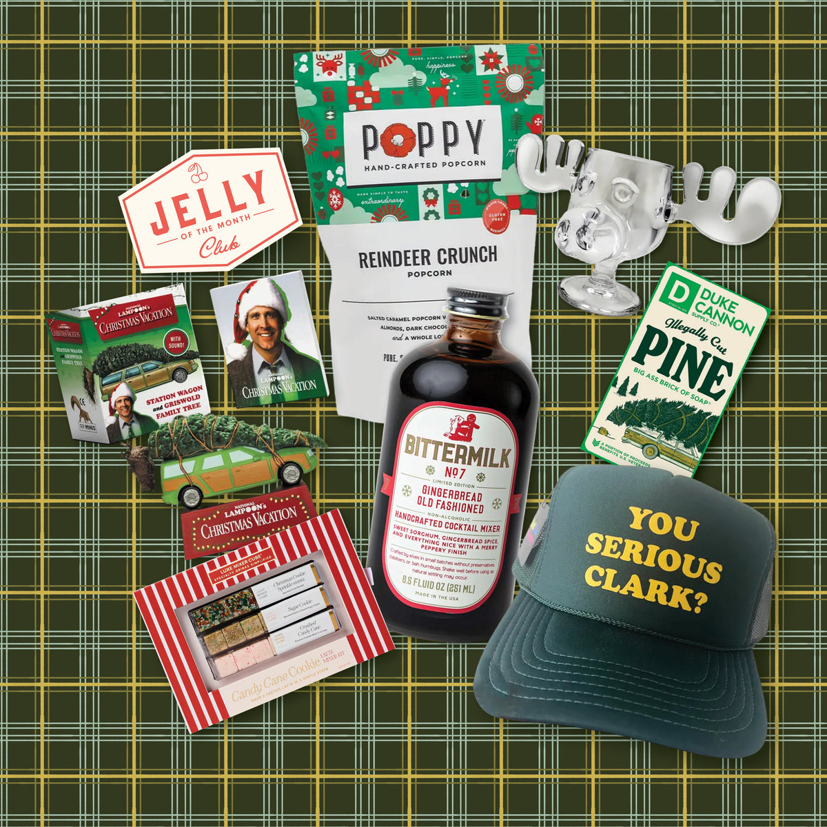 A collection of items for a Christmas Vacation theme gift box including You Serious Clark? Trucker Hat, Gingerbread Old Fashioned Cocktail Mixer, Christmas Vacation Playing Cards with Ornament, Christmas Vacation Moose Mug, Poppy Reindeer Crunch, Candy Cane Cookie Latte Mixer Kit, Jelly of the Month Club Sticker, and a Bar of Duke Cannon Pine Scented Bar Soap on a green plaid background.