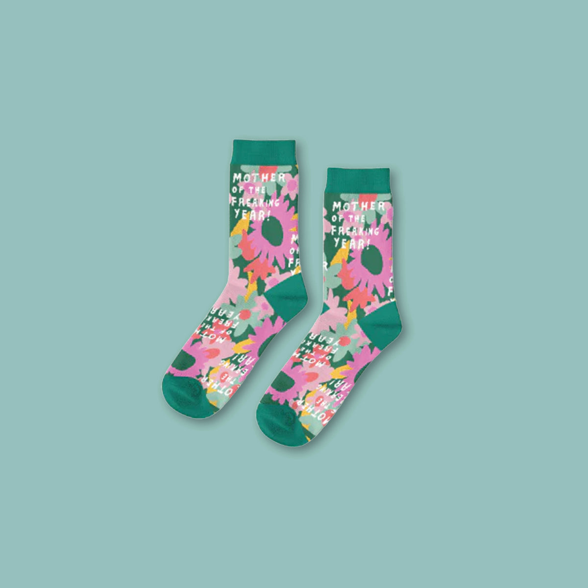 On a turquoise background sits a pair of dark teal socks with pink and yellow flowers that say "Mother of the Freaking Year!" in white writing. 