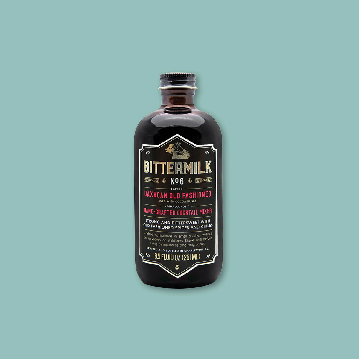On a teal background sits a dark brown bottle of Bittermilk No. 6 flavor Oaxacan Old Fashioned Handcrafted Cocktail Mixer.